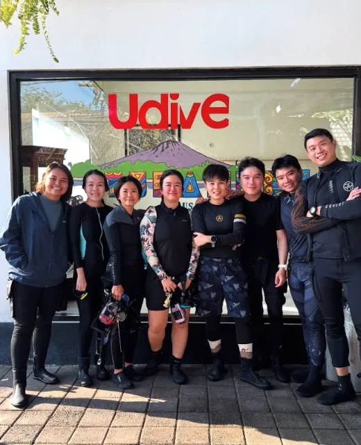 Groupe de plongeurs souriants devant la vitrine d'un centre de plongée