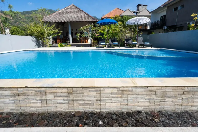 Piscine rectangulaire bleue entourée de végétation et de bâtiments