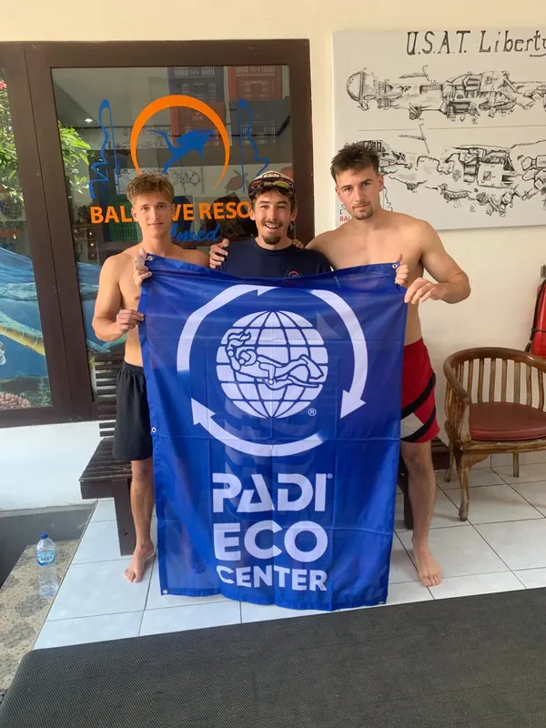 Trois jeunes adultes souriants tenant un drapeau PADI Eco Center