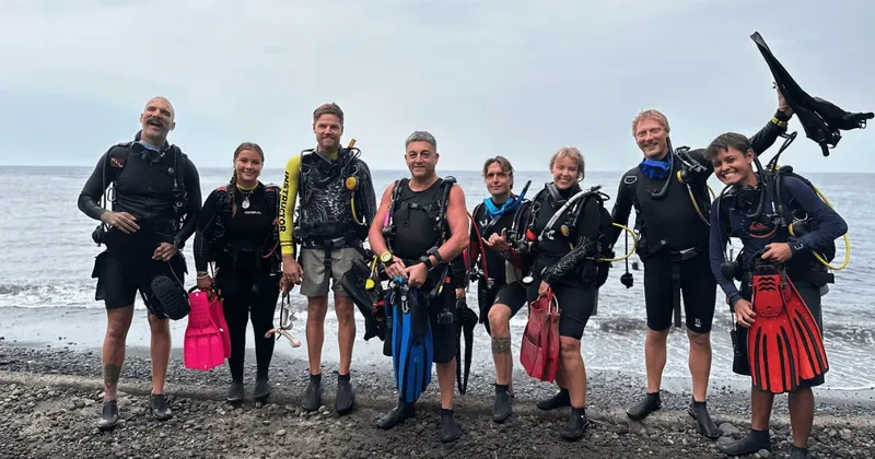 Groupe de plongeurs souriants équipés sur une plage de galets