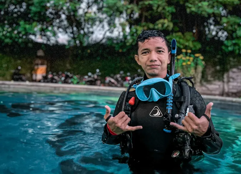 Plongeur souriant en combinaison, masque et détendeur dans une piscine