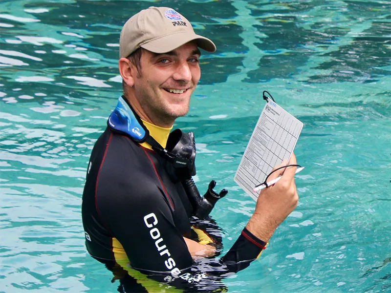 Plongeur souriant dans l'eau avec une ardoise de plongée
