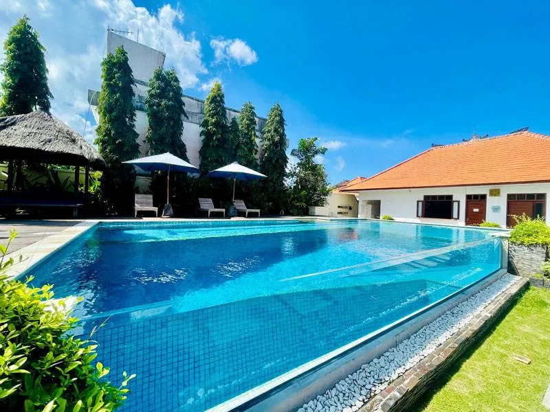 Piscine bleue entourée de végétation et bâtiments sous ciel bleu