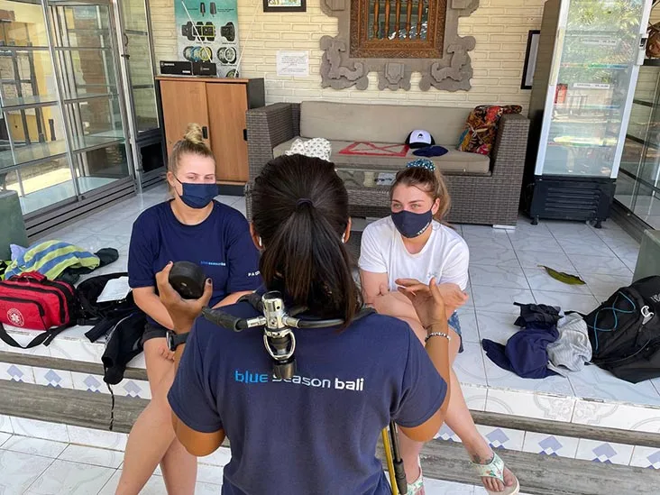 Quatre personnes discutent, équipement de plongée à proximité, extérieur d'un centre