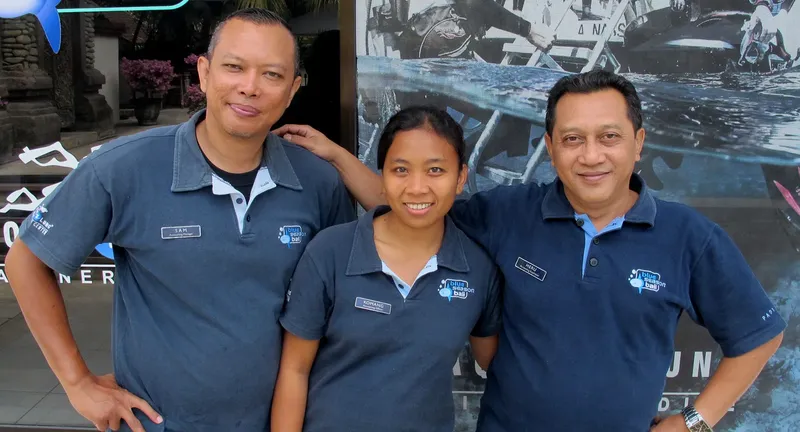 Trois personnes souriantes posent devant une grande image marine