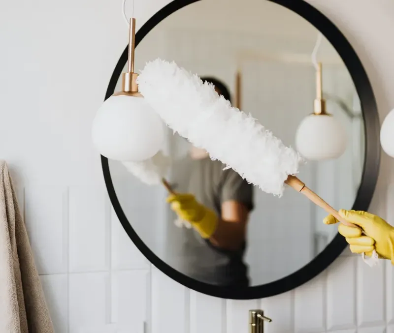 Personne en gants jaunes nettoie un miroir rond avec un plumeau