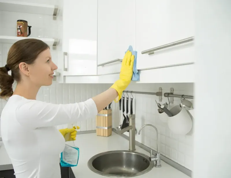 Femme souriante nettoyant les placards de cuisine avec un chiffon bleu
