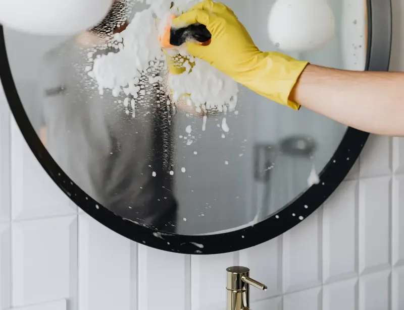 Une personne nettoie un grand miroir rond avec un chiffon jaune