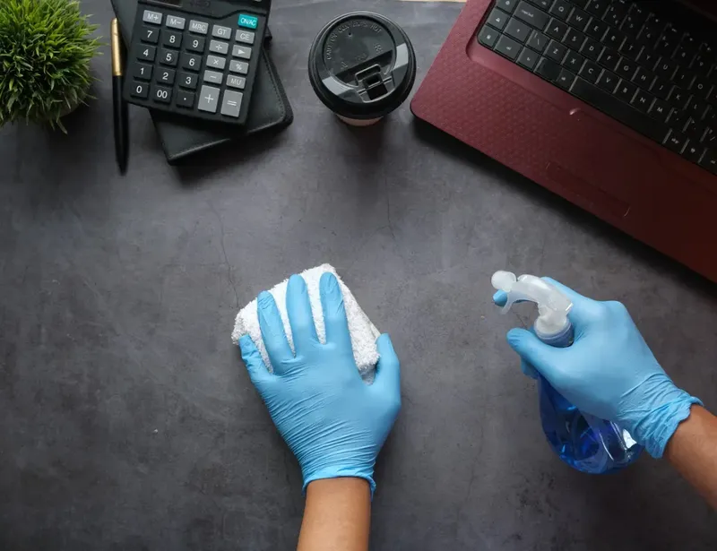 Mains gantées nettoyant une surface avec un vaporisateur et un chiffon