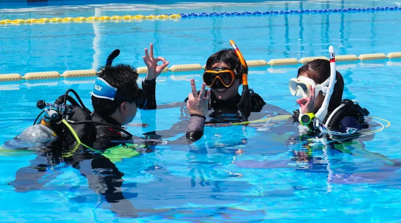 Trois plongeurs en formation dans une piscine, souriants et communicatifs