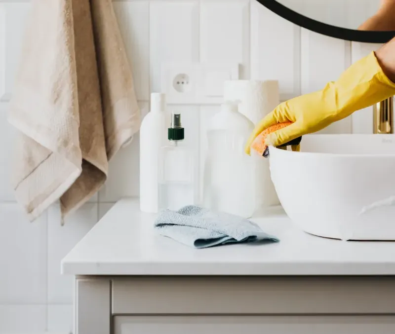 Personne en gants jaunes nettoie une salle de bain blanche et lumineuse