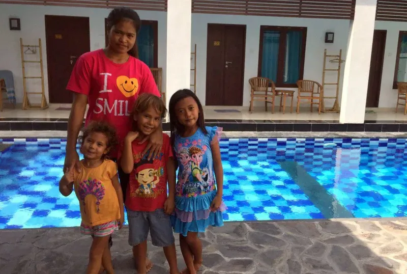 Quatre enfants et une femme sourient devant une piscine bleue