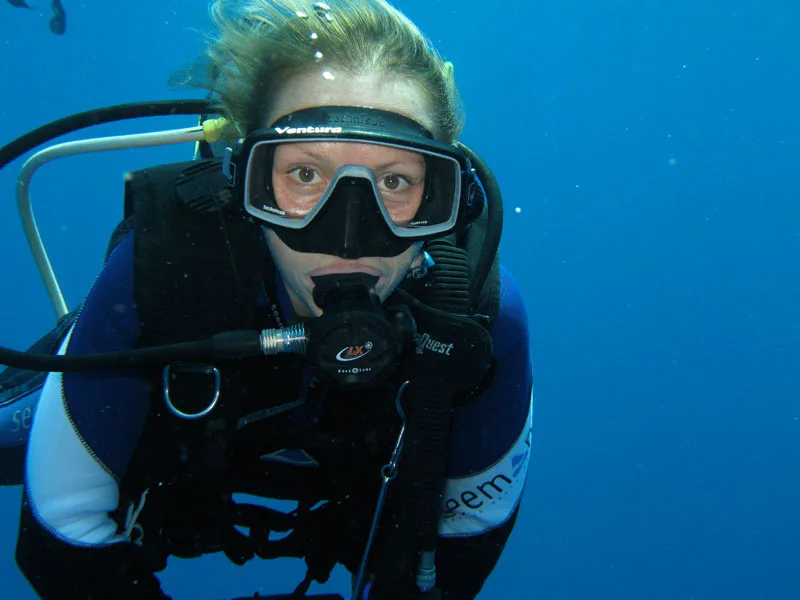 Plongeuse souriante avec masque et détendeur dans l'eau bleue