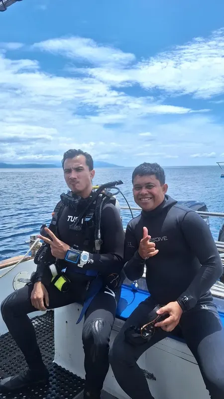 Deux plongeurs équipés sourient sur un bateau en mer