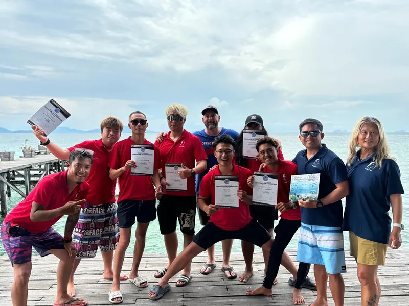 Groupe de personnes souriantes tenant des certificats sur un ponton en bois