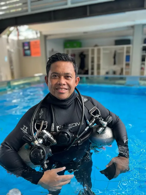 Plongeur souriant en combinaison complète dans une piscine bleue