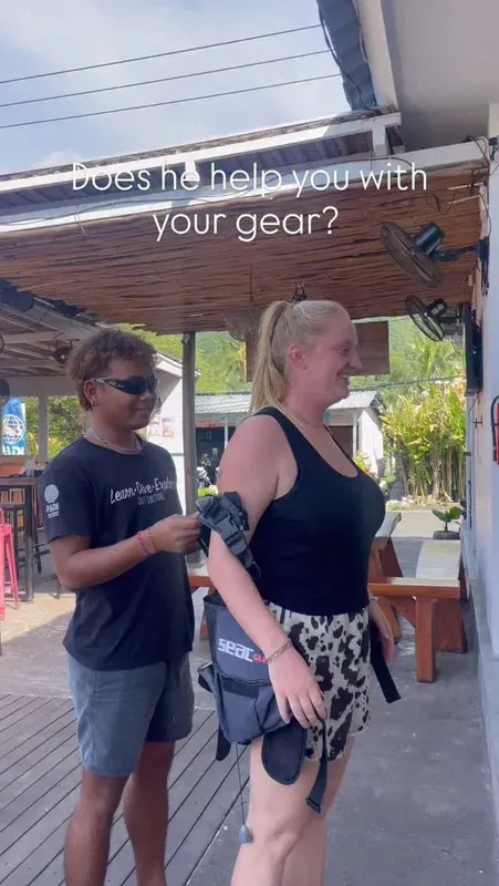 Un moniteur aide une plongeuse à enfiler son équipement de plongée