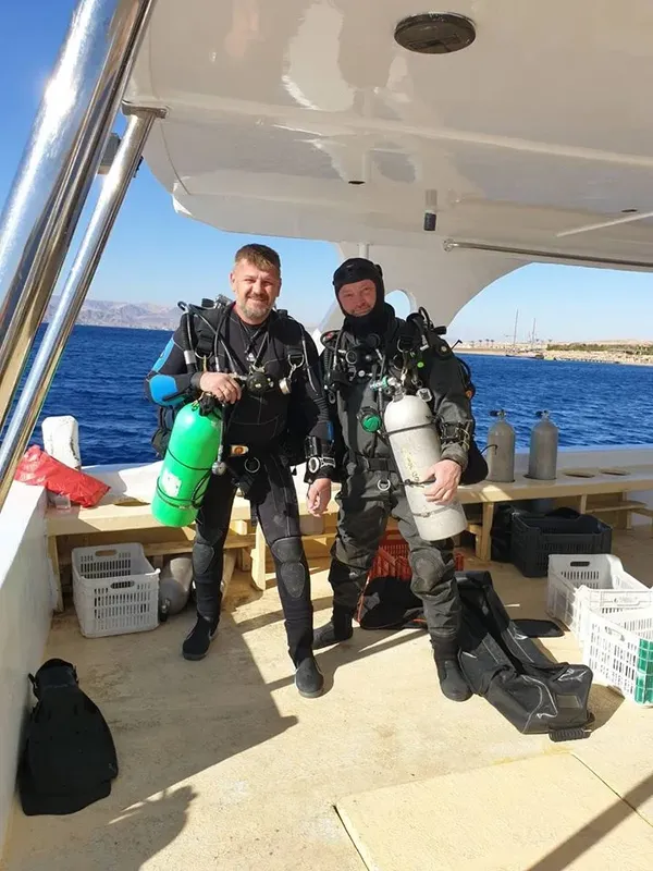 Deux plongeurs équipés sur un bateau avec la mer en arrière-plan
