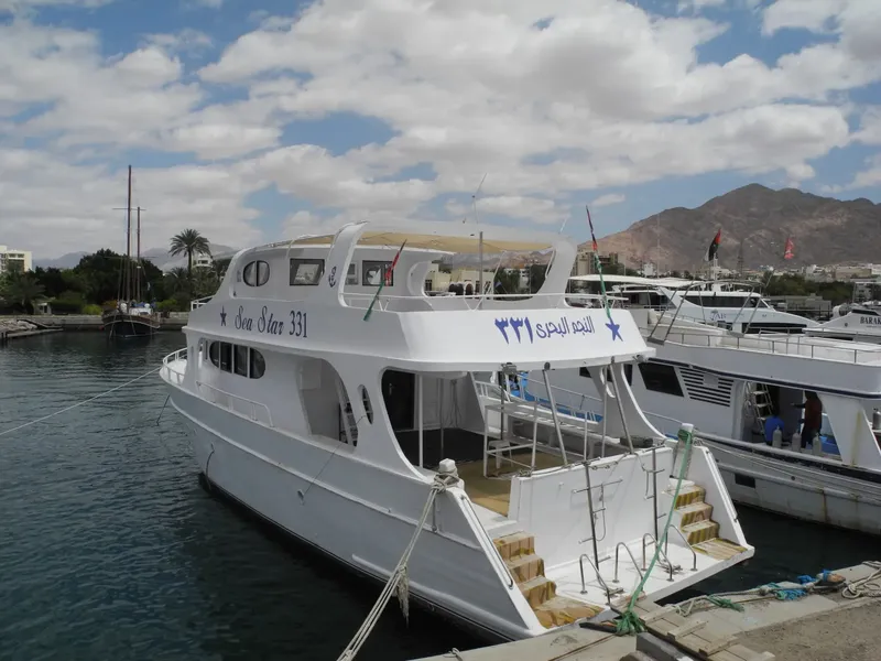 Bateau de plongée blanc amarré dans un port ensoleillé avec des montagnes