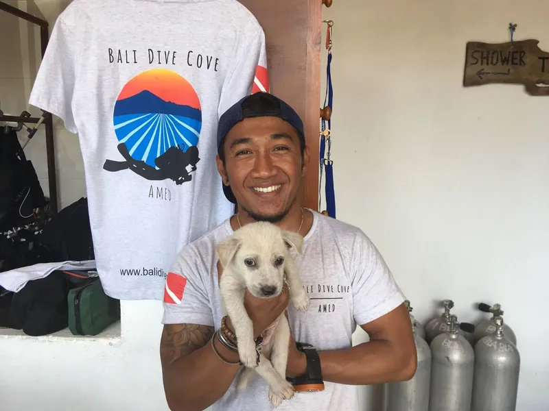 Un homme souriant tient un chiot devant des équipements de plongée