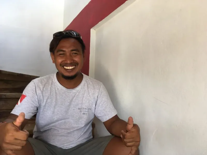 Homme souriant faisant un signe de pouce levé, assis à l'extérieur