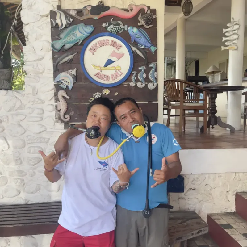 Deux hommes souriants avec du matériel de plongée devant un décor mural