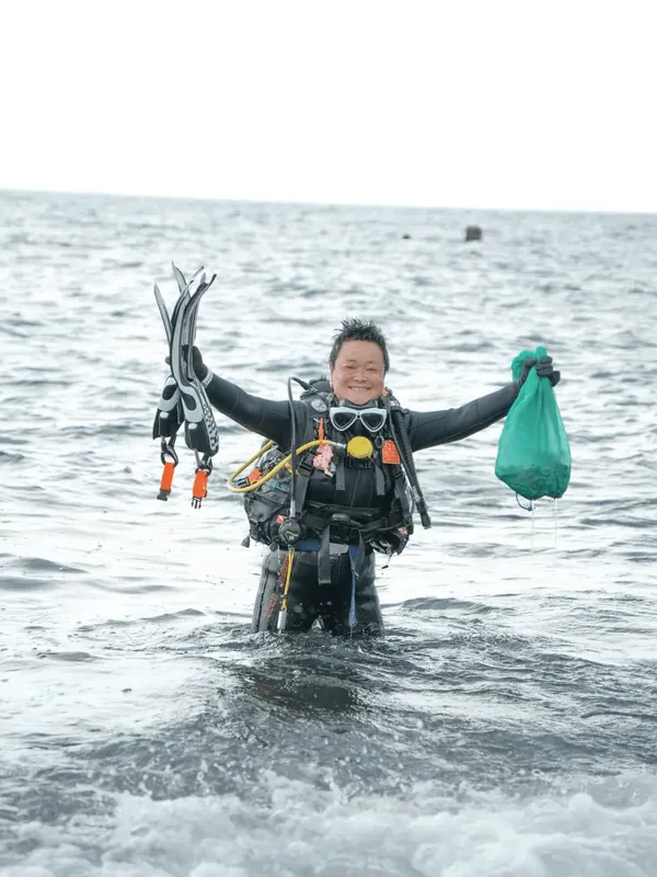 Plongeur souriant sortant de l'eau avec palmes et sac plastique