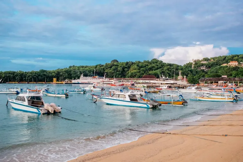 Plage avec de nombreux bateaux amarrés devant une colline verdoyante
