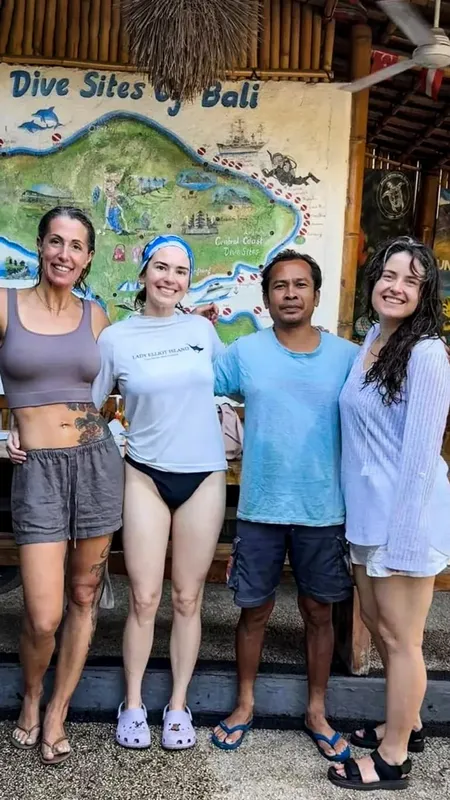 Quatre personnes souriantes posent devant une carte de Bali illustrant des sites de plongée