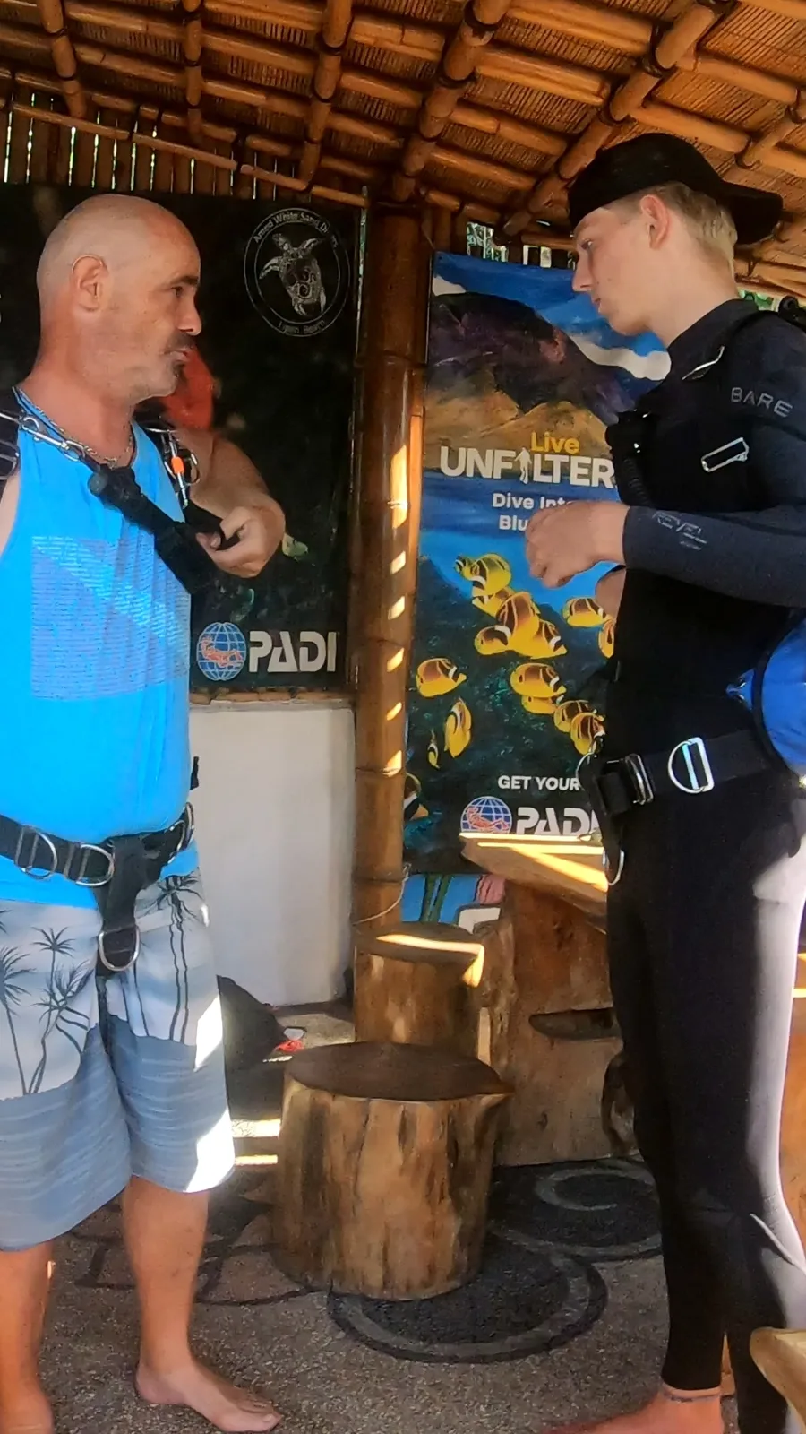 Deux hommes discutent devant une affiche de poissons tropicaux et de plongée
