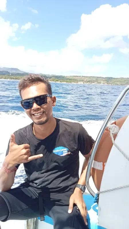 Homme souriant sur un bateau en mer, faisant un signe de la main