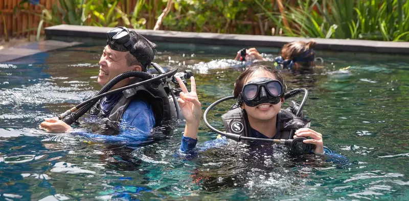 Deux plongeurs en formation dans une piscine, souriants et équipés