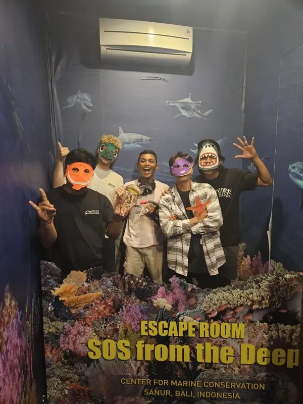 Quatre personnes souriantes avec des masques de poissons devant une affiche
