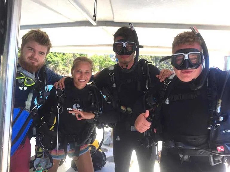 Quatre plongeurs souriants équipés prêts pour une sortie en mer