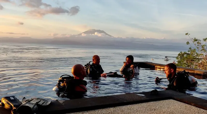 Plongeurs équipés discutent dans l'eau avec un volcan en arrière-plan