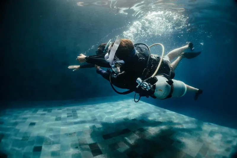 Deux plongeurs en combinaison s'entraînent dans une piscine bleue claire