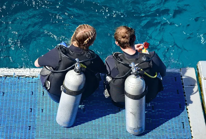 Deux plongeurs assis au bord du ponton, préparant leur matériel
