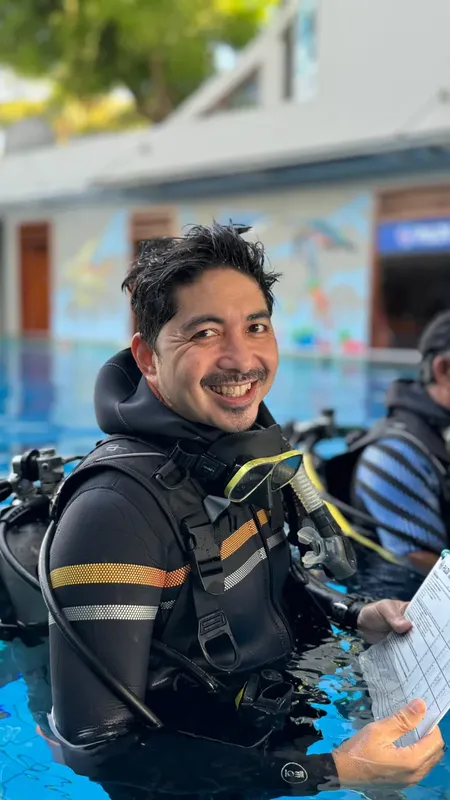 Plongeur souriant avec son équipement près d'une piscine et d'un bâtiment