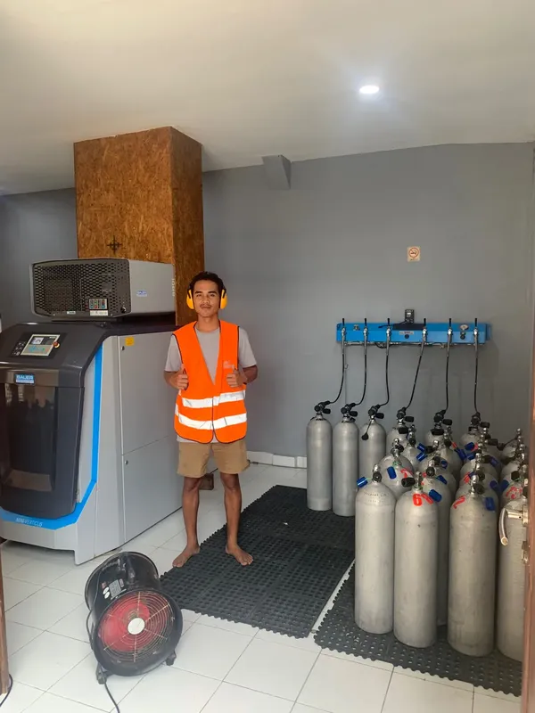 Un homme en gilet de sauvetage devant des bouteilles de plongée