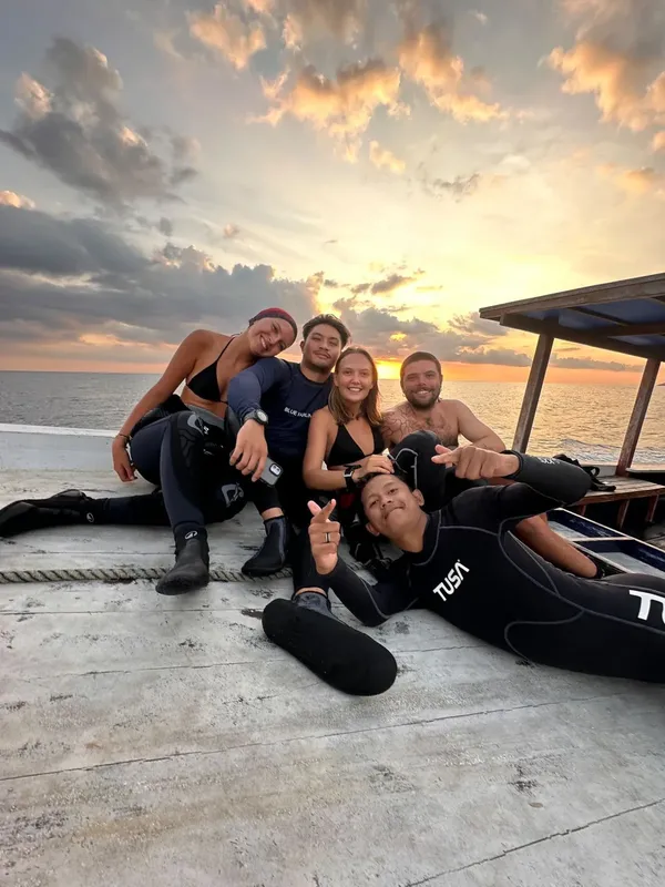 Groupe de plongeurs souriants sur un quai au coucher du soleil