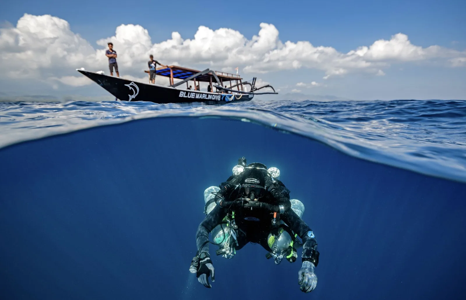 Plongeur en immersion sous un bateau traditionnel avec un ciel nuageux