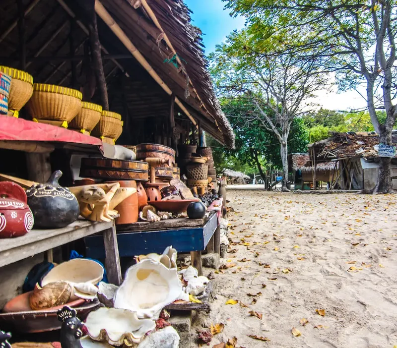 Artisanat local exposé sur des étagères devant des huttes traditionnelles