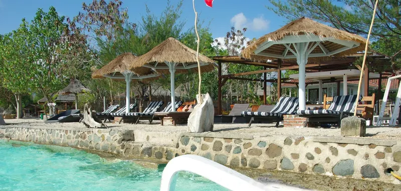 Terrasse avec parasols de chaume, transats et bâtiments en arrière-plan