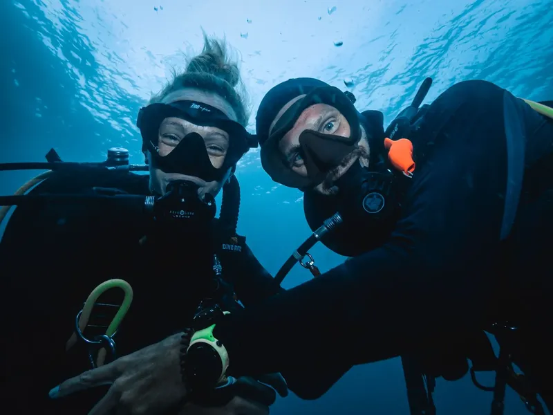 Deux plongeurs souriants avec leur équipement, prise de vue sous-marine