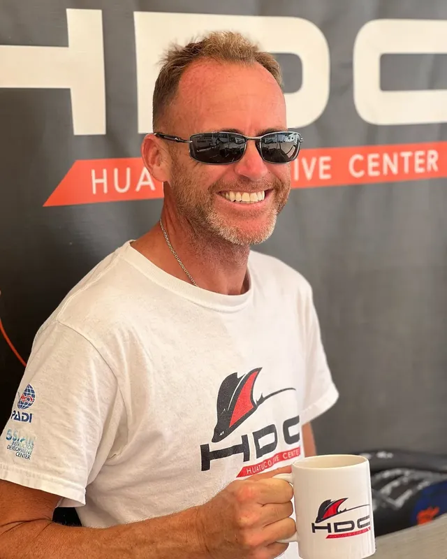 Homme souriant avec lunettes de soleil tenant une tasse blanche