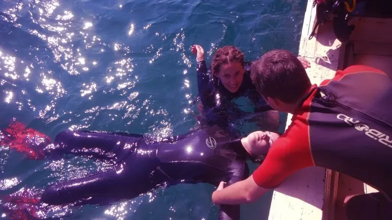 Plongeuse sortant de l'eau aidée par un membre d'équipage sur bateau