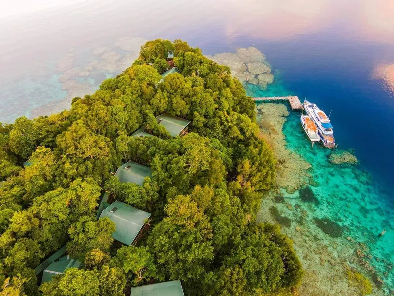 Île tropicale avec bungalows, bateau de plongée et eau turquoise claire