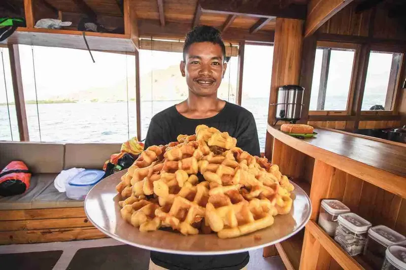 Un homme souriant présente une grande assiette de beignets dorés