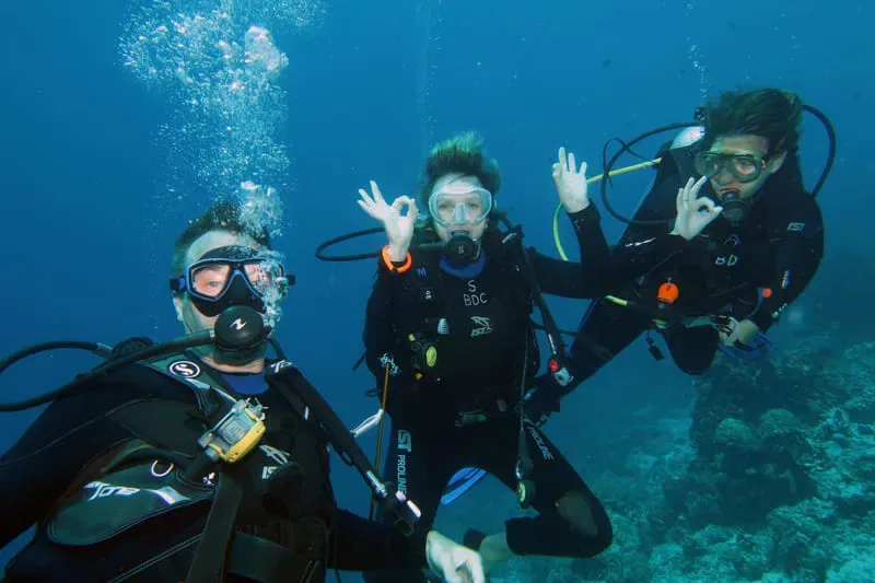 Trois plongeurs souriants font le signe OK sous l'eau bleue