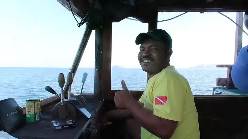 Homme souriant à bord d'un bateau, pouce levé, mer calme